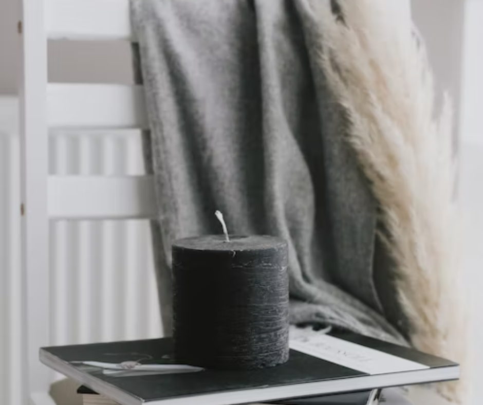 White chair with a grey blanket and a white fluffy blanket draped over the back of. A grey candle sits on the seat of the chair. 