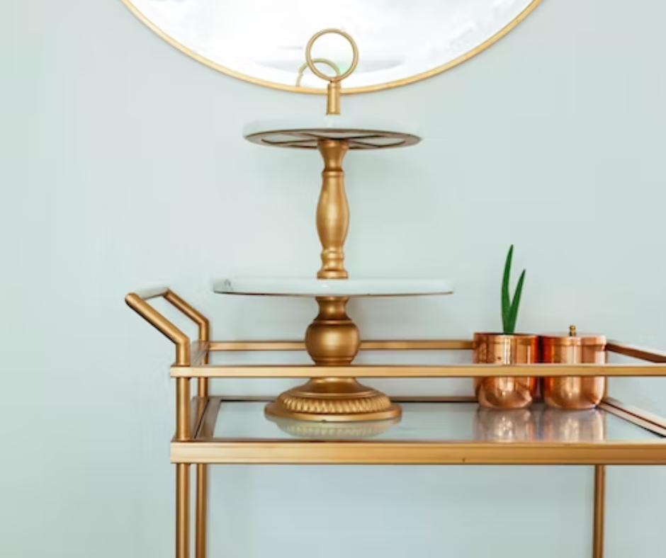 Brass bar cart with glass top with a brass display stand and copper containers displayed on top.