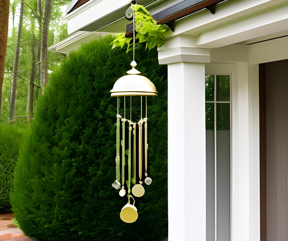 A metal windchime hangs outside next to a white pillar near the front door of a home.